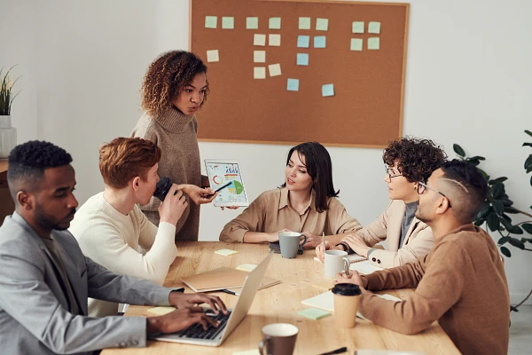 A group of colleagues is having a discussion during a meeting, with one person presenting information on a tablet.